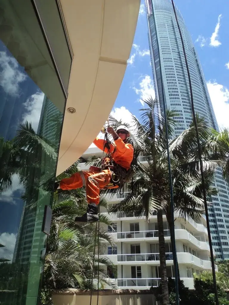 On ropes among the palms, Technician in orange overalls on a tower.