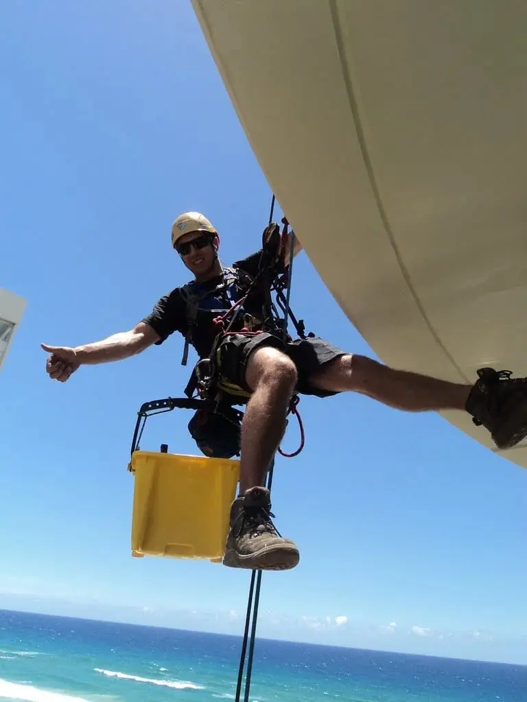 Above the beach, Technician on ropes, ocean below.