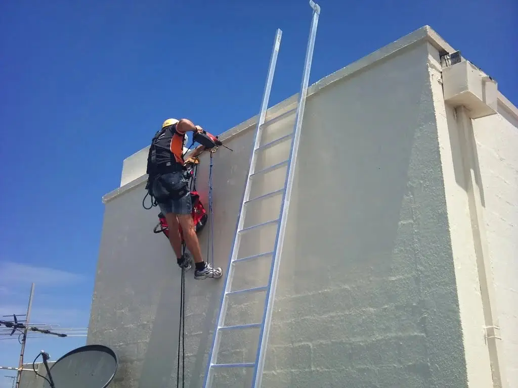 Fixing a new ladder, Roped technician drilling at a parapet.