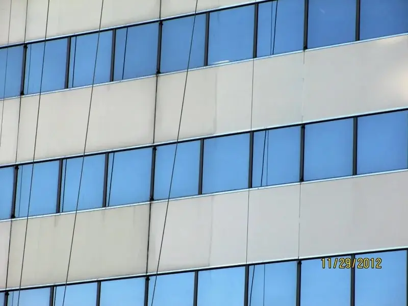 Weathered facade panels, Pale facade panels between bands of blue-tinted windows, with streaking and marks on the panels and ropes hanging down the face.