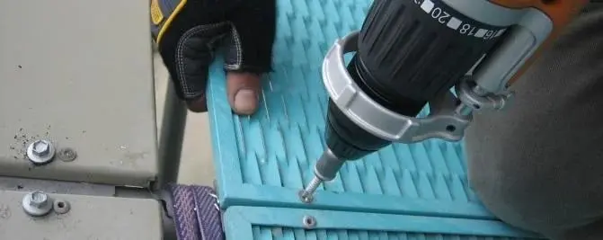 Fixing a sunshade panel, A gloved hand holding a turquoise slatted panel while a cordless drill drives in a screw.