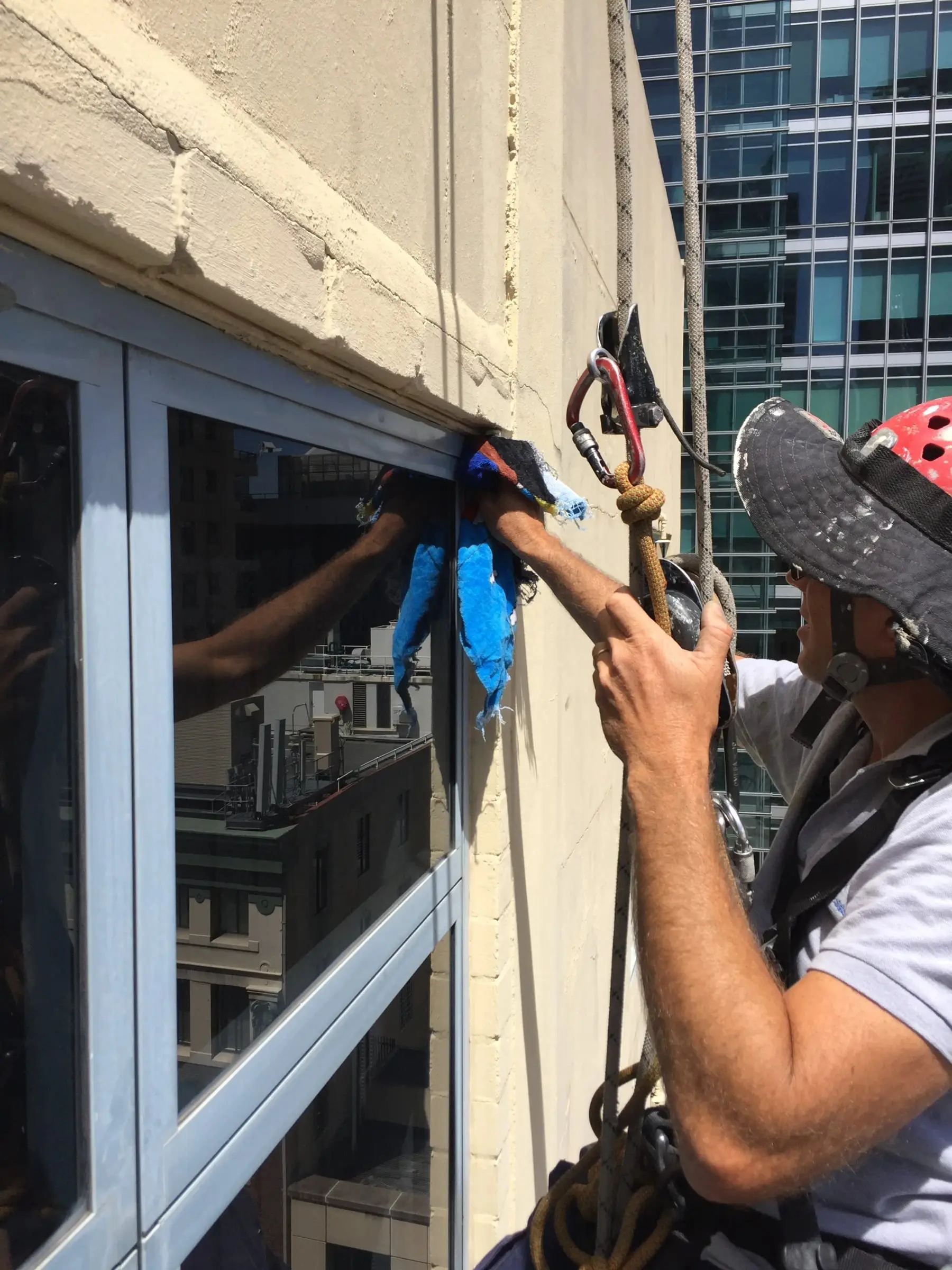 Technician on ropes sealing a window frame, 350 Kent St, Sydney