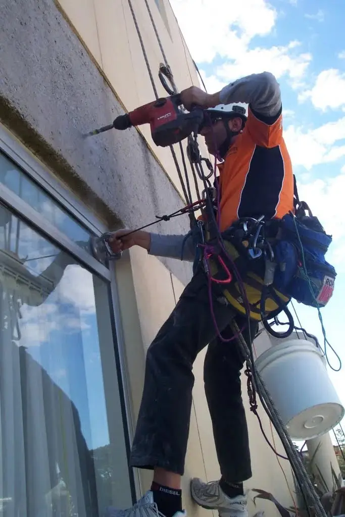 OneVision technician on ropes drilling beside a window, Glenavy, Cronulla
