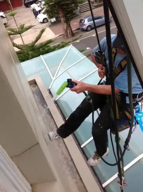 OneVision technician on ropes water testing a window above a glass roof, Peninsula, Manly