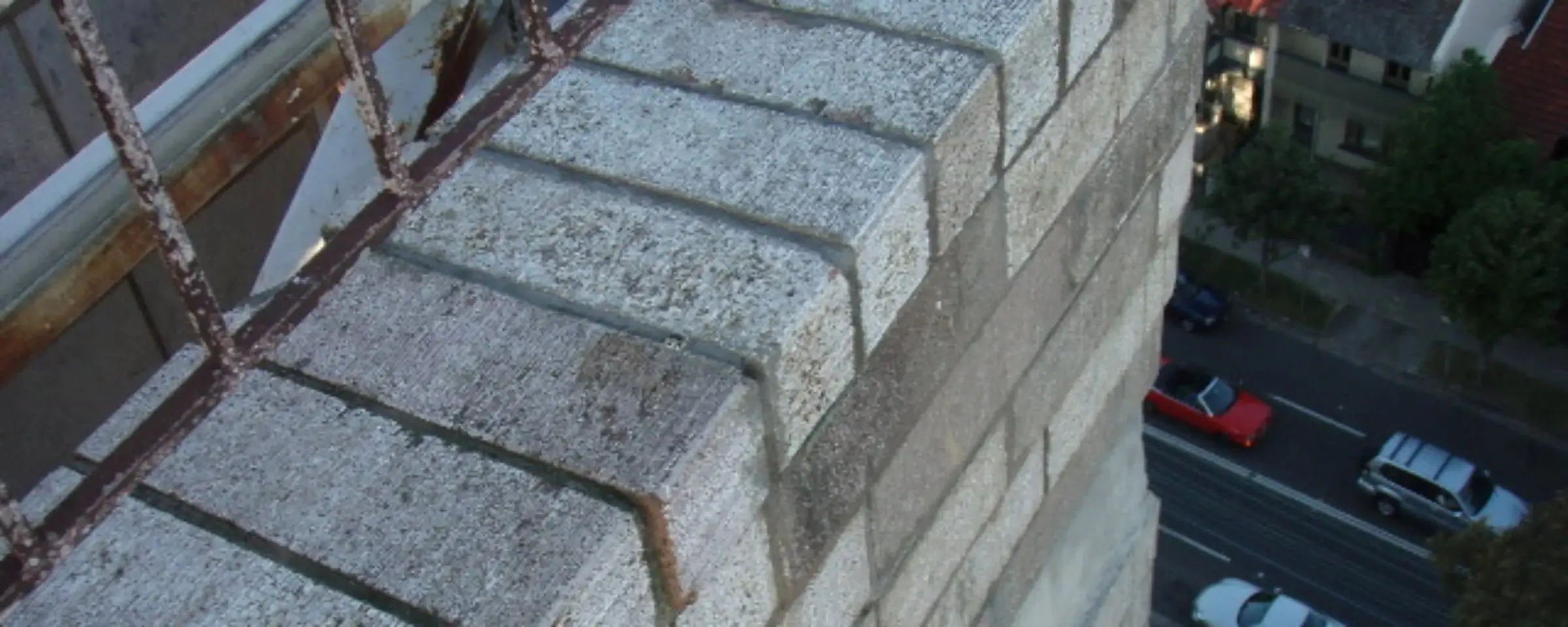 Parapet brickwork, A brick parapet high above a street, seen from above beside a rusted metal balustrade.