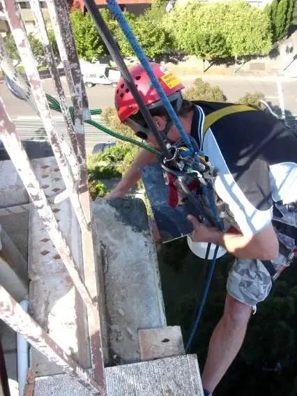 Working on ropes, A rope access technician in a red helmet working on the top of a brick parapet, high above the street.