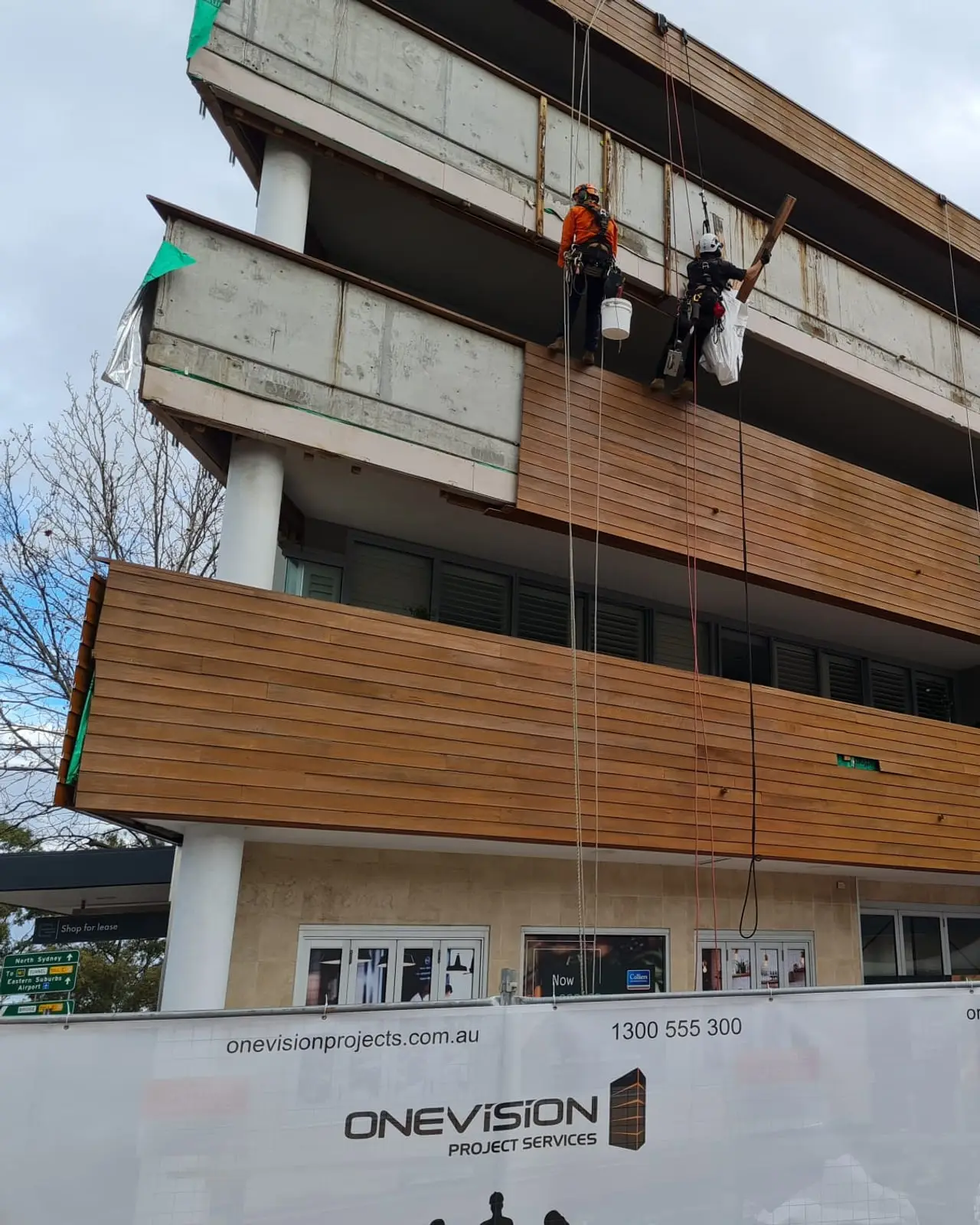 Building D at Cammeray Square during the works: two rope access technicians on the facade, with the old cladding stripped back to bare concrete on the upper balconies