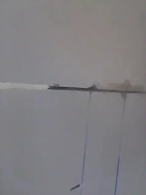 Joints being sealed, Horizontal and vertical joints on a painted wall, filled with grey sealant.