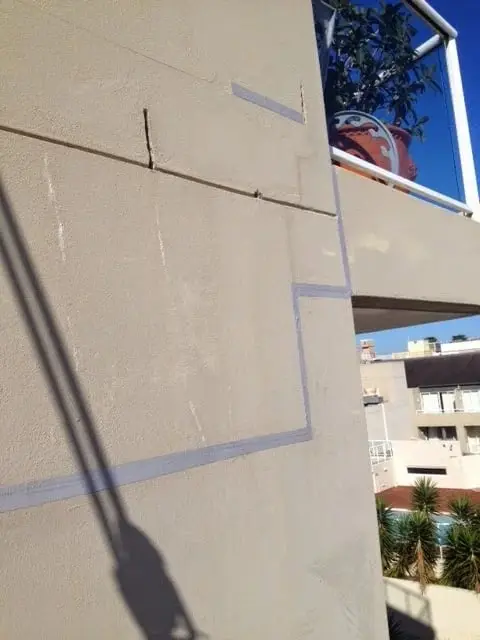 Joints on a facade, Cracks and grey sealed joints running across a painted facade next to a balcony.