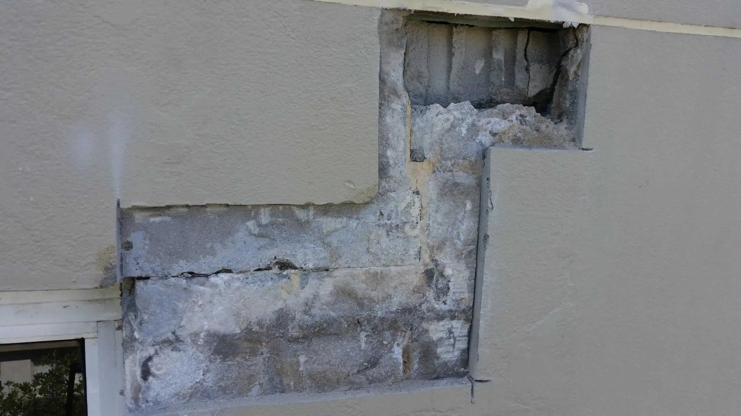 Damaged concrete cut out, A painted wall above a window with the damaged concrete cut back in a stepped section, ready for repair.