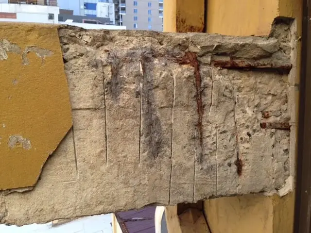 Spalled beam before repair, A painted concrete beam with the spalled concrete cut away, showing rusted reinforcing bars.