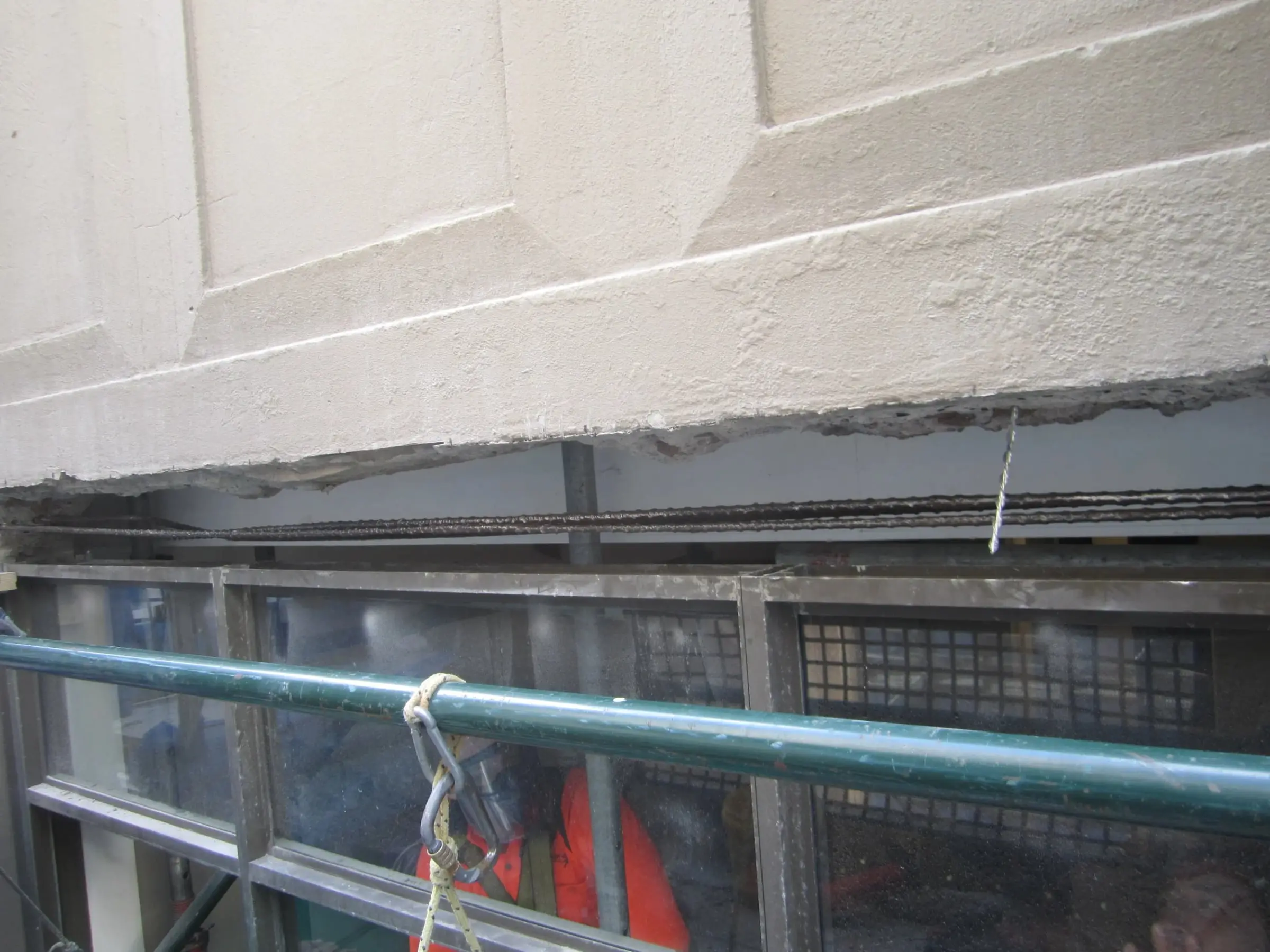 Reinforcement exposed, A long concrete beam above a window cut back along its underside to expose the corroded reinforcing bars.