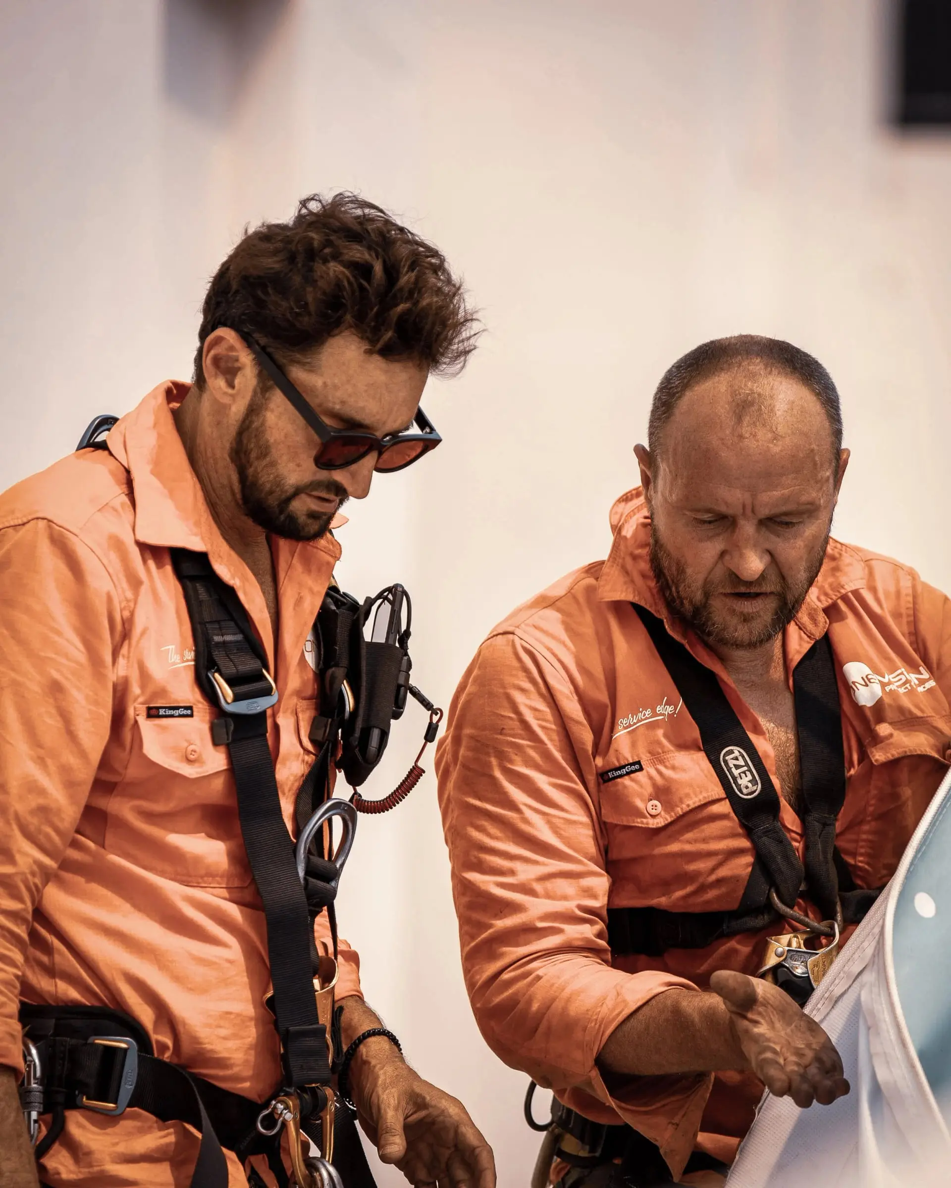 Two OneVision rope access technicians in orange shirts checking their harnesses