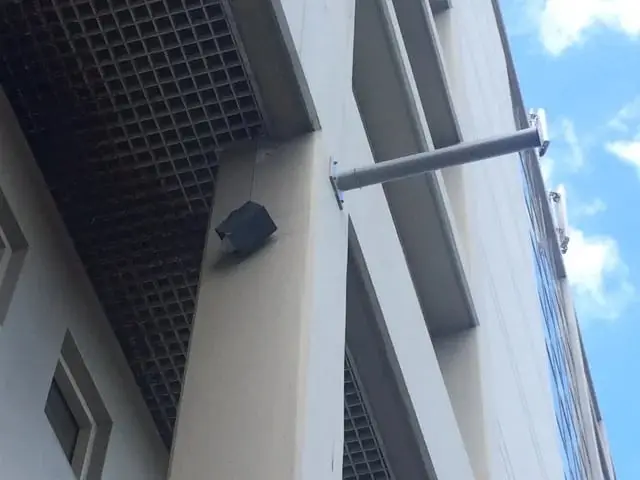 Fittings on the facade, A light fitting and a banner arm mounted high on a pale facade column under a grid ceiling.