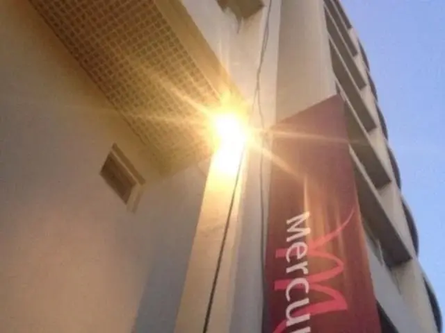 Light fitting at height, A bright light on a facade column beside a red Mercure banner, looking up at the building.