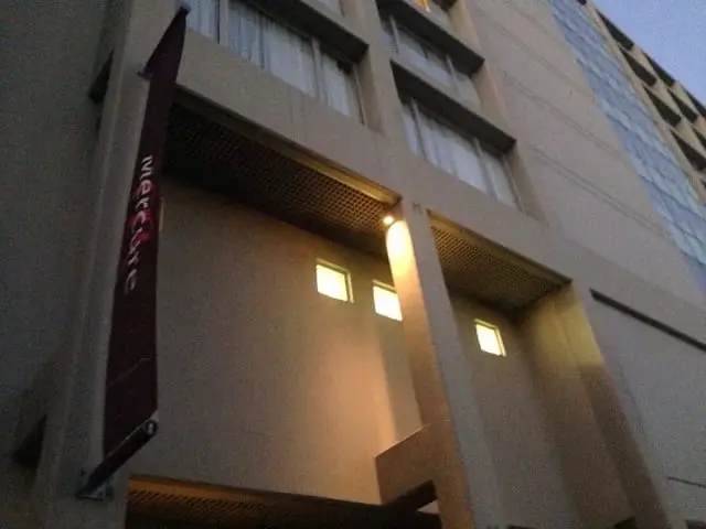 Lit facade at dusk, Lights under a facade overhang glowing beside a hanging Mercure banner.