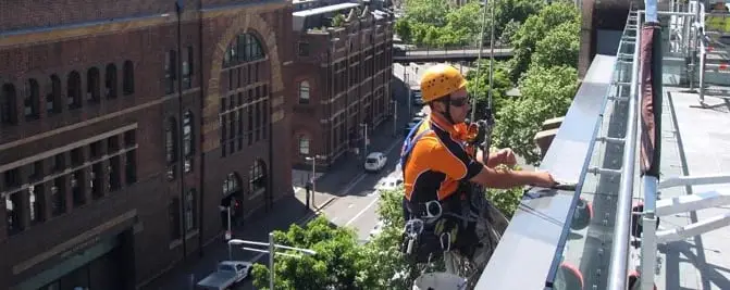 Going over the edge, A technician rigging at a rooftop edge above the street.