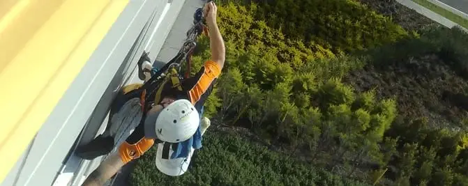 Working the facade, A roped technician seen from above, over garden beds.