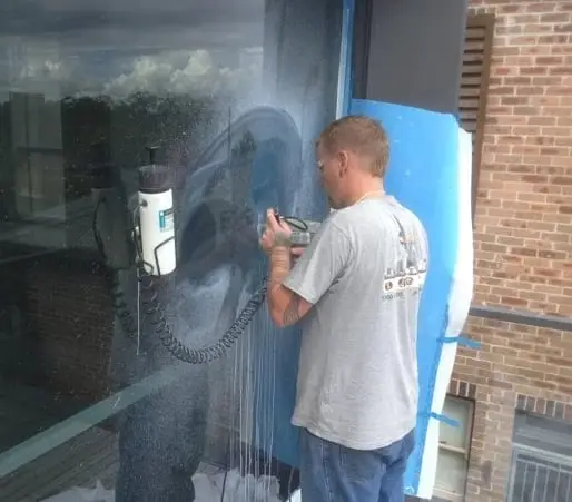 Polishing out damage, A technician machine-polishing a large glass panel, with the surrounding area masked off in blue.