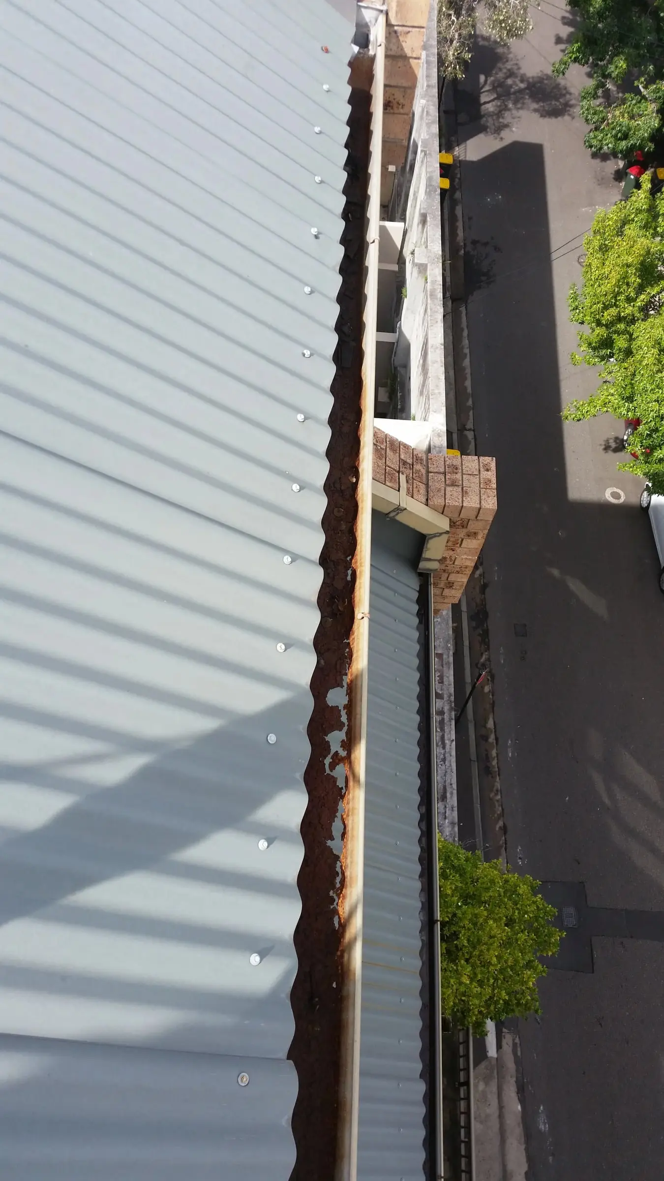 Gutter from the roof edge, Looking down a gutter along the edge of a corrugated roof, several storeys above the street.