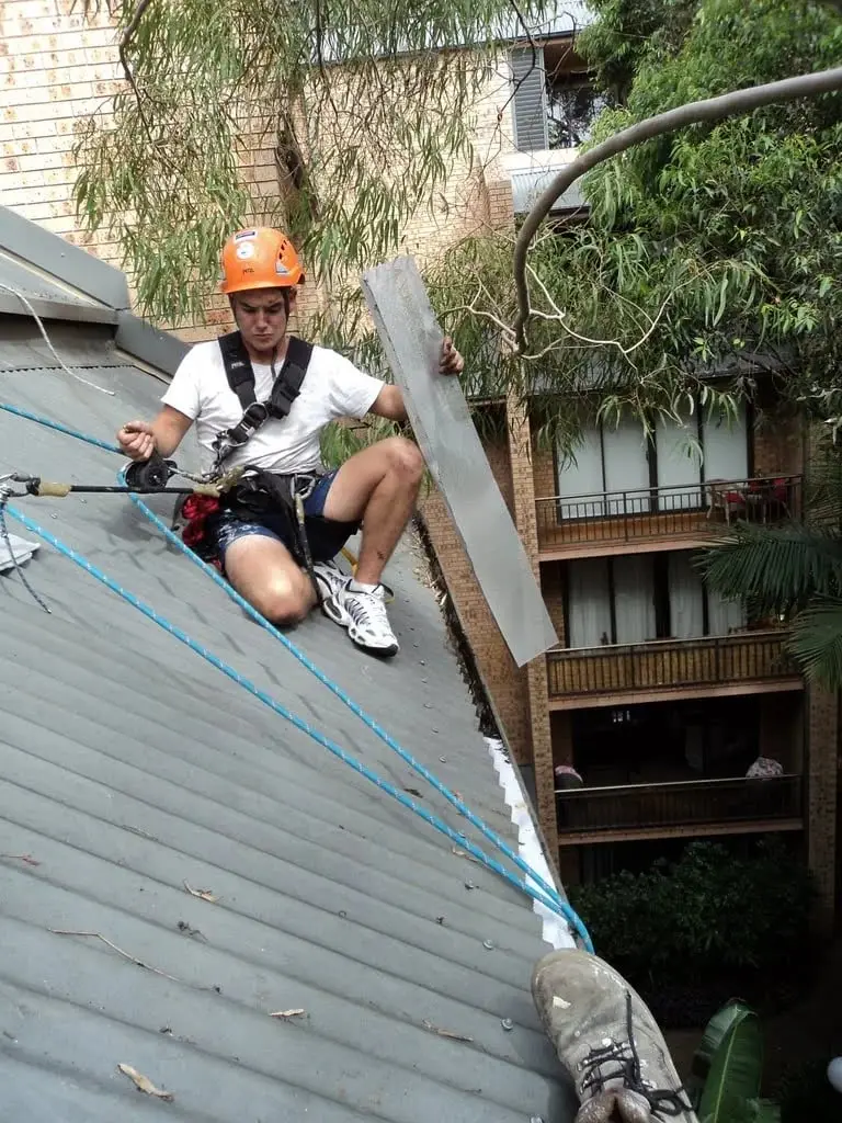 Rope access on the roof, A technician in a helmet and harness on a roof, holding a length of new metal flashing.