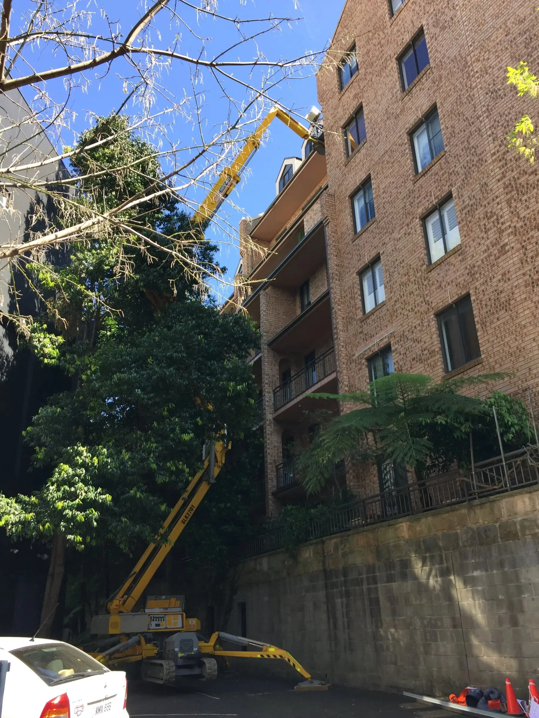 Boom lift on site, A boom lift set up in a driveway beside a multi-storey brick apartment building.