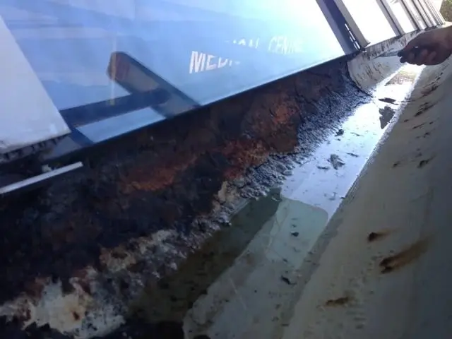 Rusted commercial gutter, A long metal gutter above a shopfront awning, lined with rust and packed debris.
