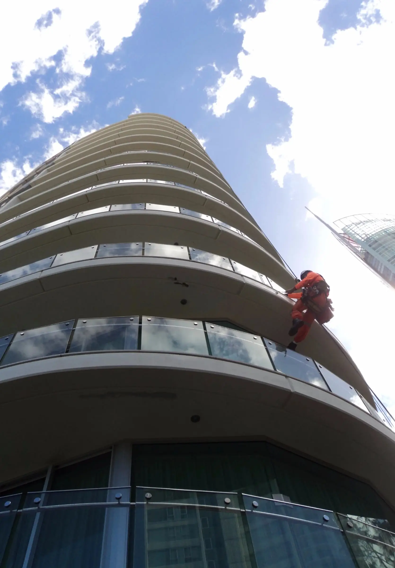 Painting on ropes, A rope access painter working on the curved balcony edges of a high-rise tower, seen from below.