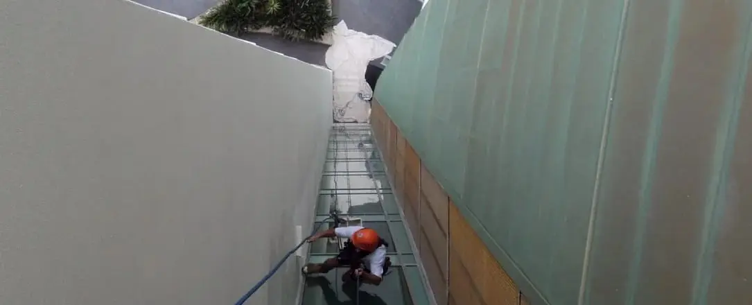 Painting between walls, A roped painter working in the narrow gap between a painted wall and a glass wall.