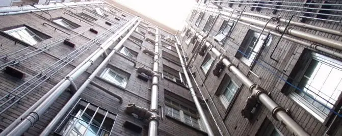 Downpipes on a high-rise, Metal downpipes and pipework running up the brick facades of two apartment buildings, seen from below.