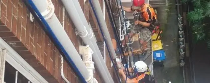 Downpipe work on ropes, Two rope access technicians working on a run of white downpipes down a brick building.
