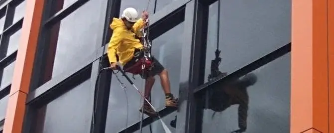 Washing the glass, A technician in a raincoat washing a glass facade.