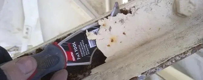 Scraping back loose paint, A scraper lifting flaking white paint off a rusted steel member.