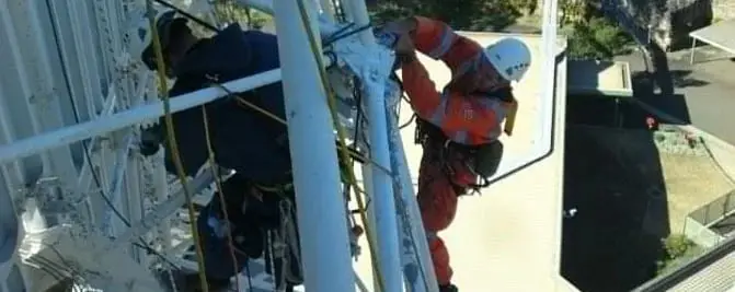 Rust repairs at height, Two rope access technicians working on a white steel lattice structure above a rooftop.