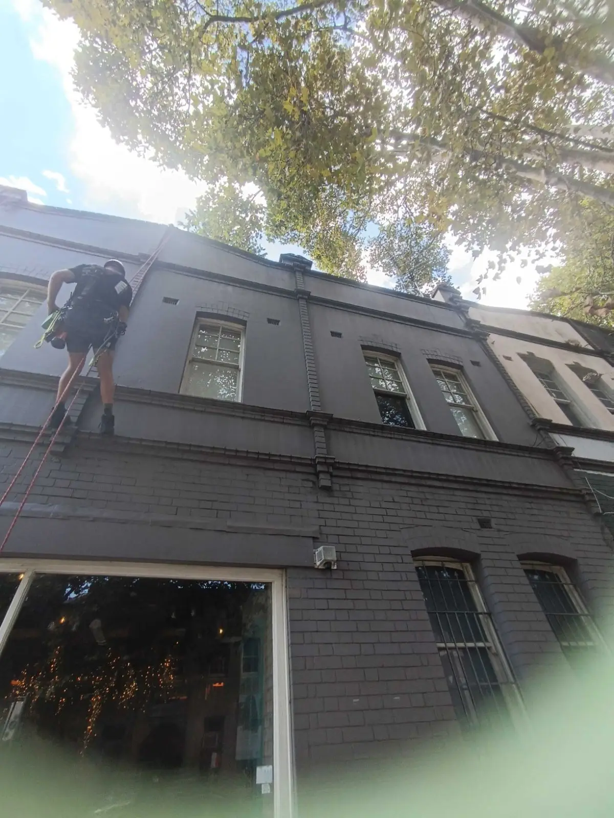 Rope access technician on the painted facade of a two-storey terrace above a shopfront
