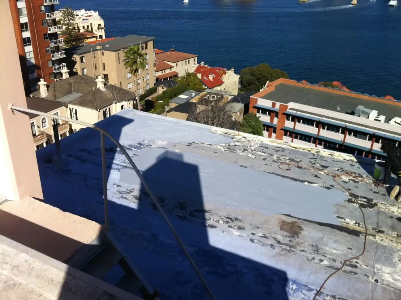 Before, failed coating, An old roof coating worn through and patchy, with the harbour behind.