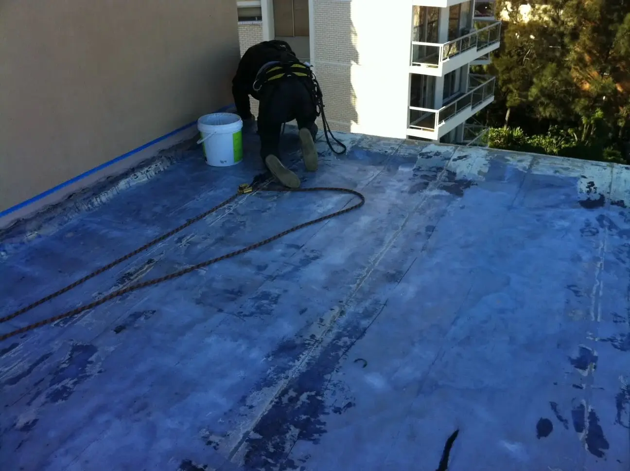 During, preparing the roof, A technician on hands and knees preparing the roof surface, with the edges masked off in blue tape.