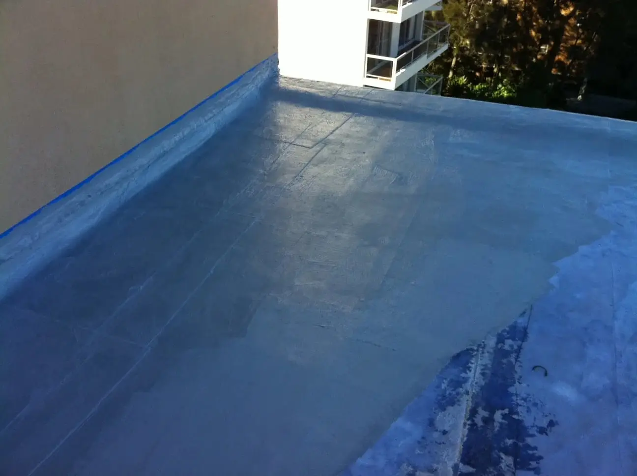 During, new coat going on, A fresh coat of membrane spreading across the prepared roof, taped along the wall line.