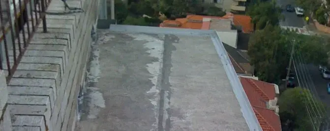Flat roof after repair, A flat roof with patched sections along its length, seen from a balcony above.