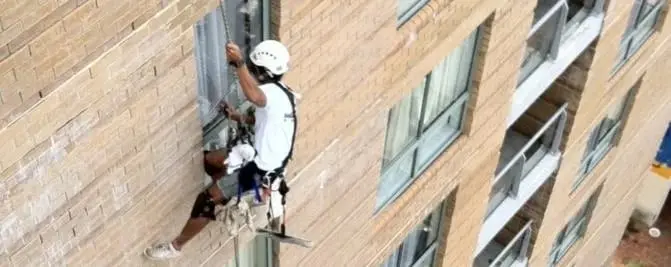 Brick apartment block, A roped technician at a window on a brick building.