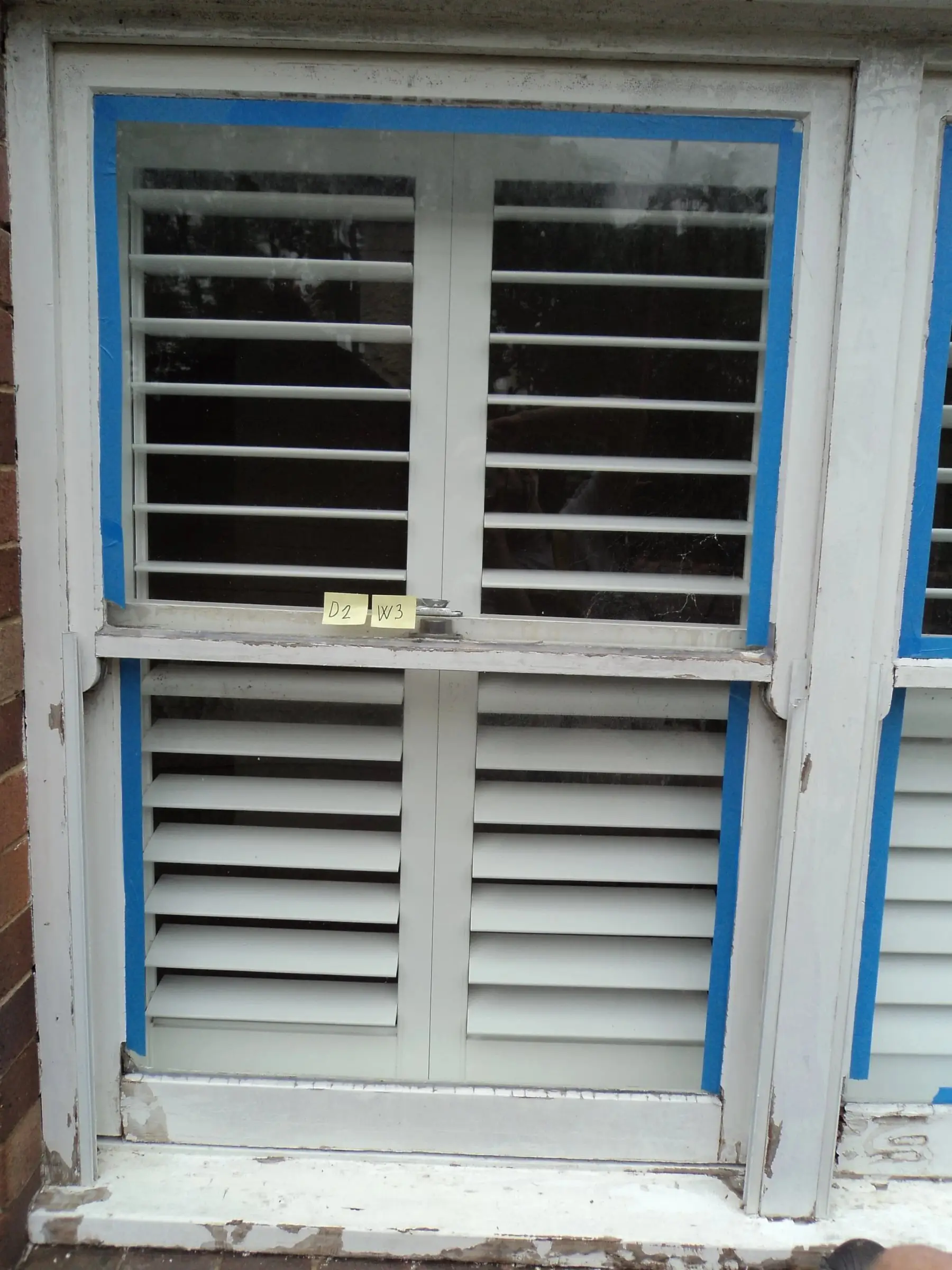 Sash window masked, A double-hung timber window with its glass edges taped in blue, ready for preparation.